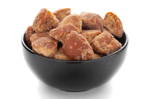 Close-Up of organic sugarcane jaggery piece in black ceramic bowl over white background